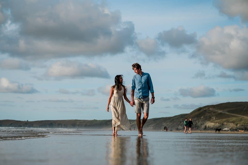 Engaged couple walking along Perranporth beach