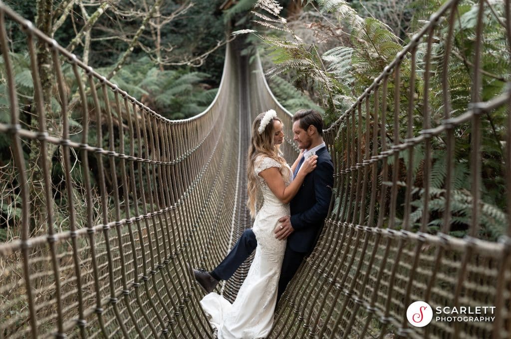 Eloping couple take a moment on the swing bridge at the lost gardens of heligan