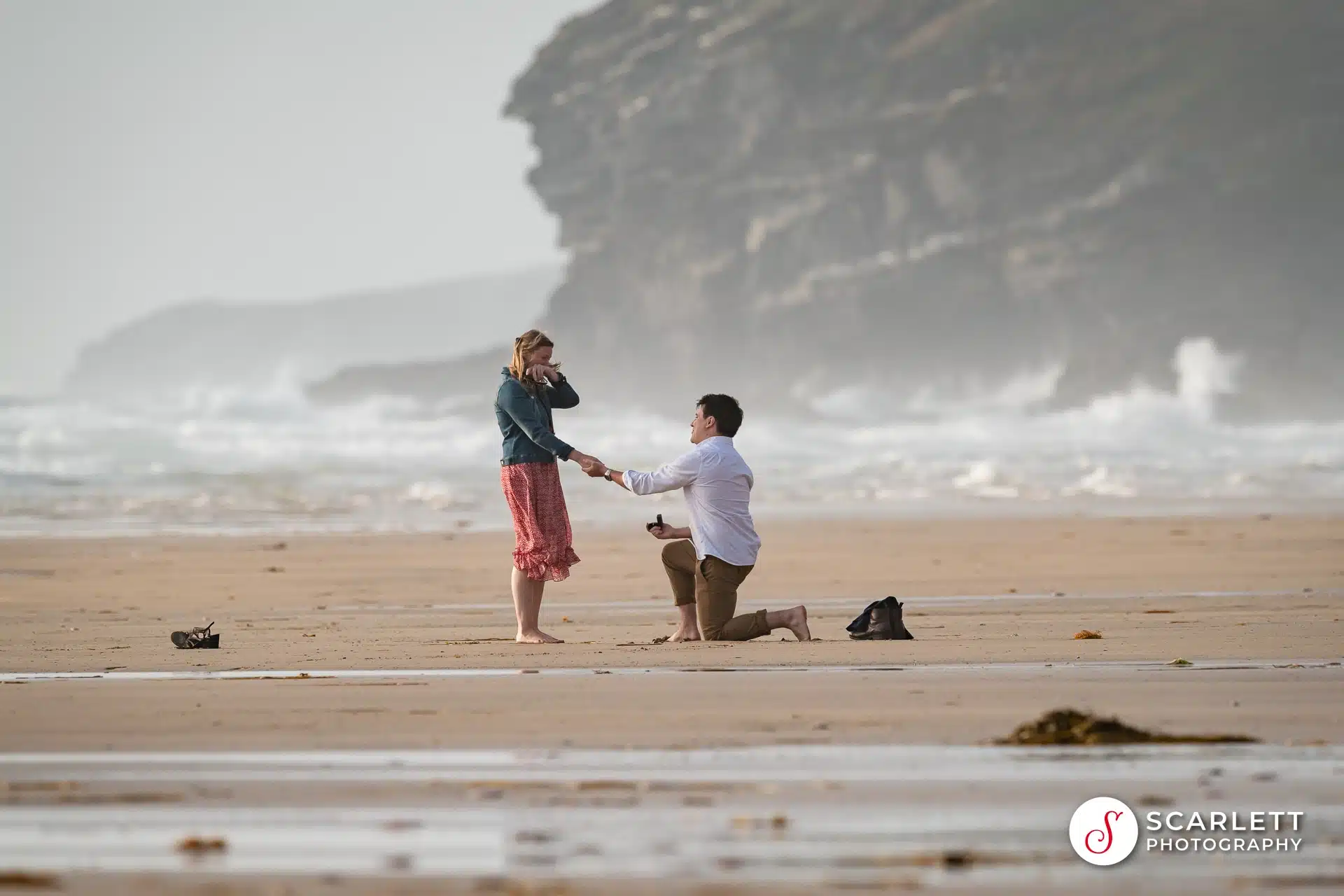 The moment she accepts his proposal at the dramatic Watergate Bay. Waves crashing against the dramatic cliffs in the background. She puts her arm in front of her face to hide the tears of happiness.