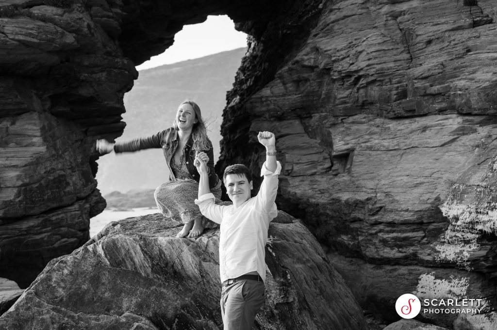 black and white image of happy couple with fist in the air after successful proposal at Watergate Bay near Newquay