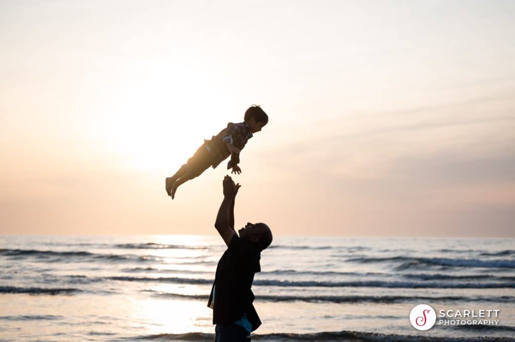 dad throws his son in the air at a family photoshoot at Lusty Glaze beach in Newquay