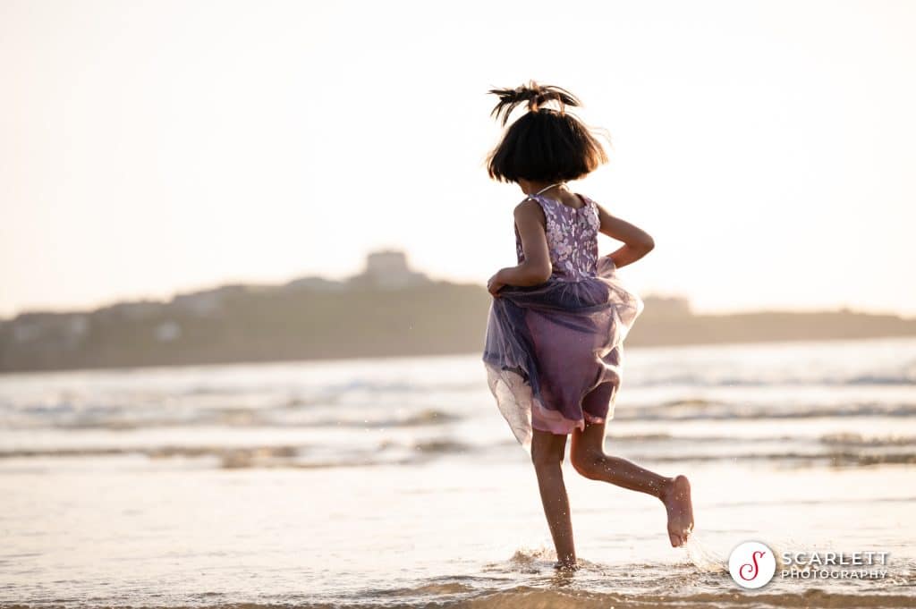 A little girl runs into the sea on a family photoshoot at Lusty Glaze beach near Newquay