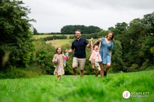 Family take a summer stroll holding hands and swinging child on some green fields in Cornwall