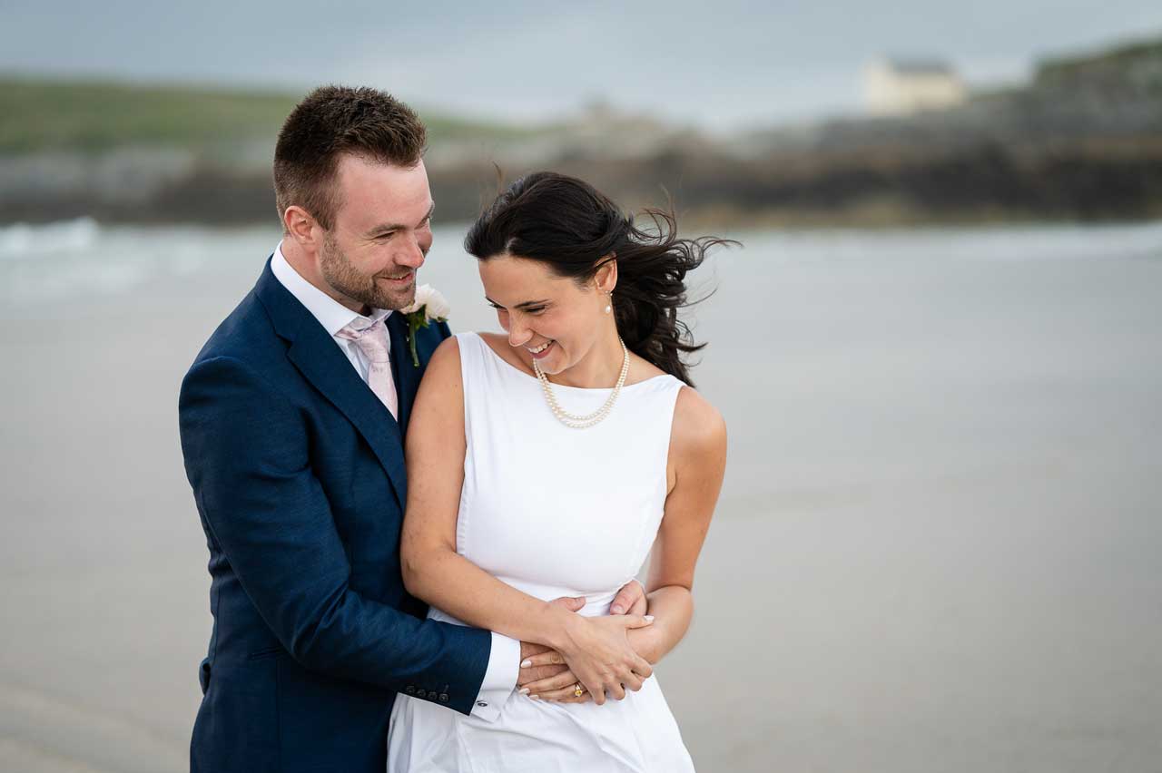 Newly married couple naturally embrace on Fistral Beach in Cornwall